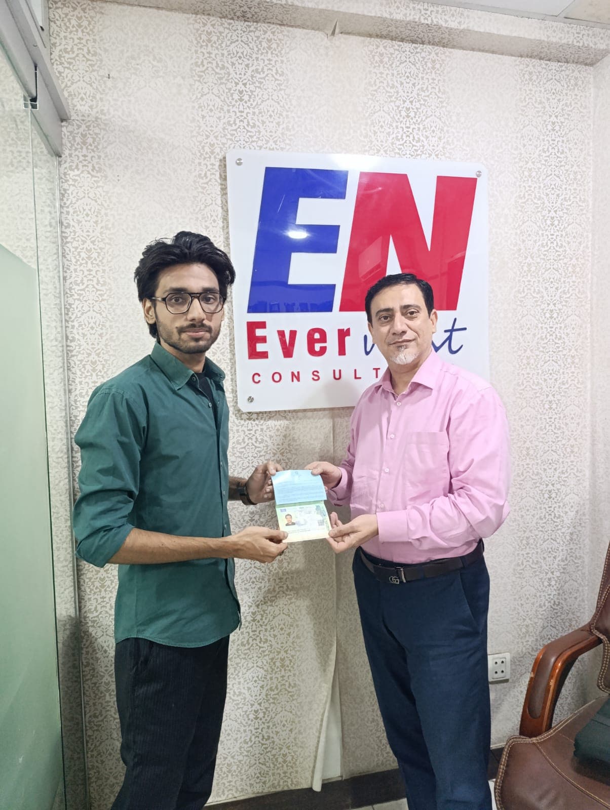 Saim Khalid in a green shirt and glasses with Sir Raza holding his Italian student visa